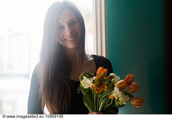 Portrait of young woman at home  holding flowers  smiling