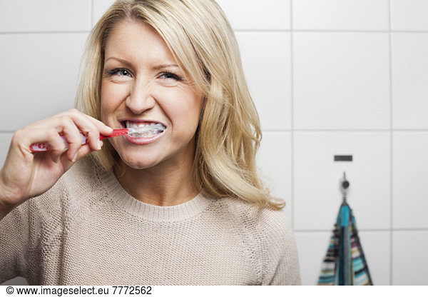 Portrait of young woman brushing teeth in domestic bathroom