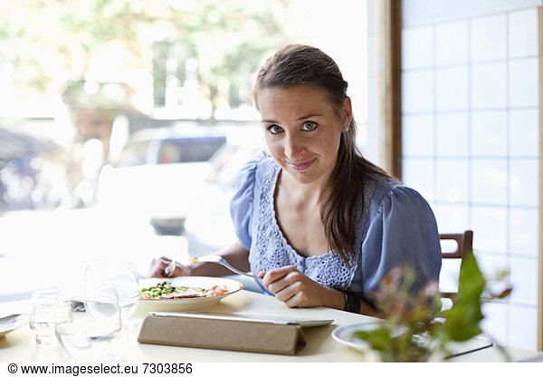 Portrait of young woman having meal while using digital tablet at restaurant table