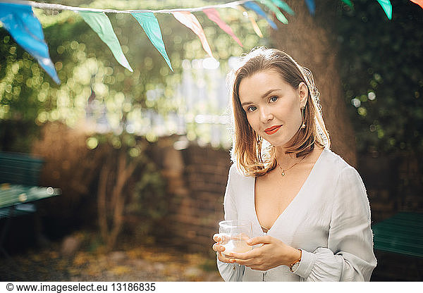 Portrait of young woman holding drink while standing in backyard