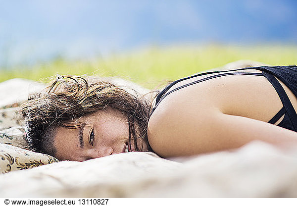 Portrait of young woman lying on textile on field