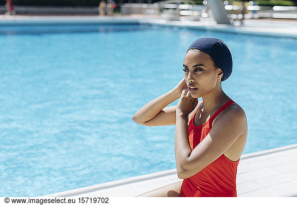 Portrait of young woman putting on swimming cap at poolside