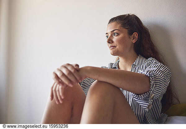 Portrait of young woman sitting on bed looking at distance