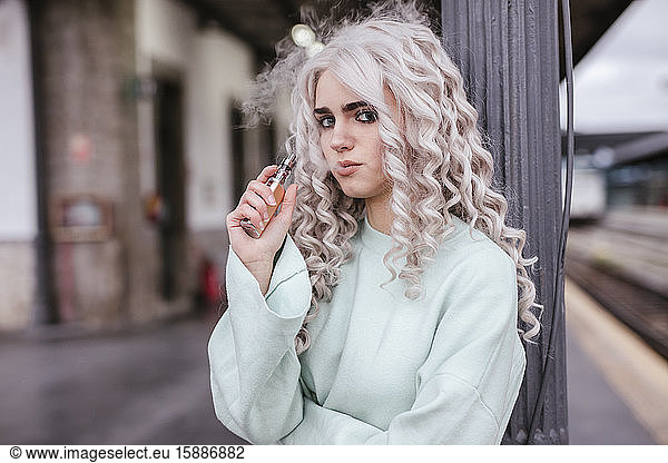Portrait of young woman smoking electronic cigarette on platform