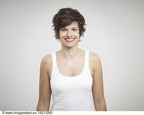 Portrait of young woman standing against white background  smiling