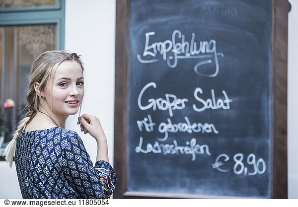 Portrait of young woman standing in front of chalkboard menu