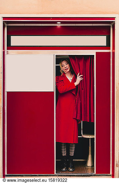 Portrait of young woman wearing red coat standing in a photo booth