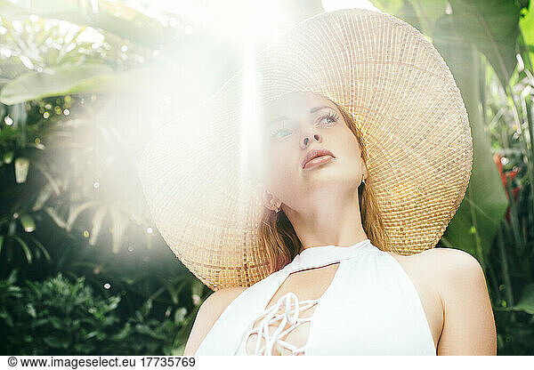 Portrait of young woman wearing straw hat illuminated by sunlight