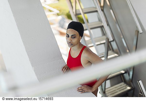 Portrait of young woman wearing swimming cap and red bathsuit standing on stairs of highboard