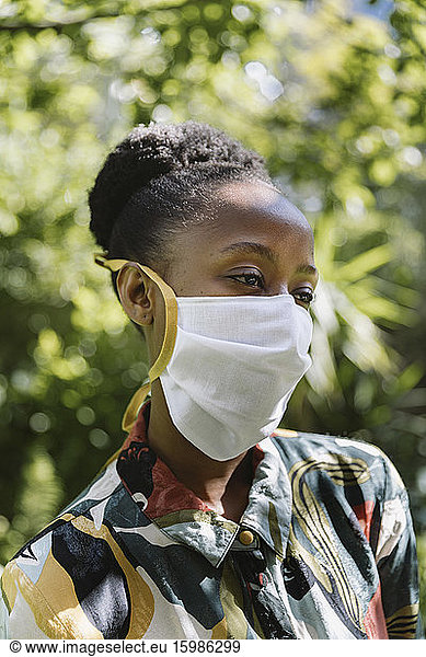 Portrait of young woman wearing white textile protective mask in garden