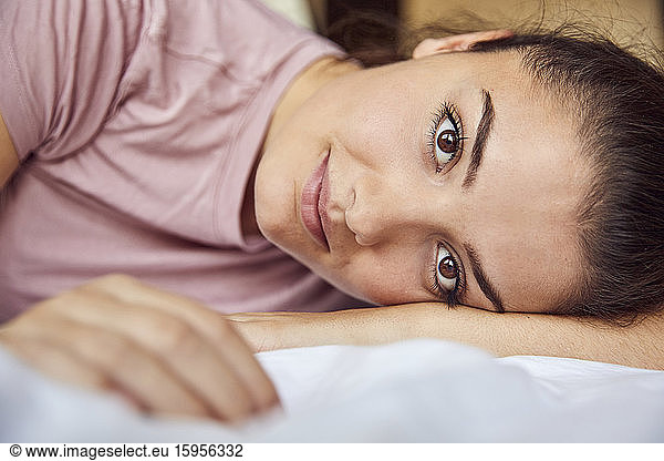 Portrait of young woman with brown eyes lying on bed