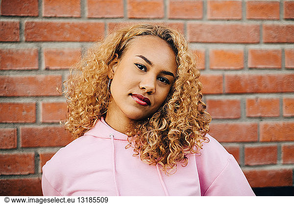 Portrait of young woman with curly hair against brick wall