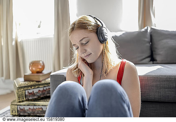 Portrait of young woman with eyes closed sitting on the floor at home listening music with headphones