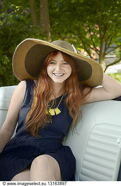 Portrait of young woman with long red hair in back seat of vintage convertible