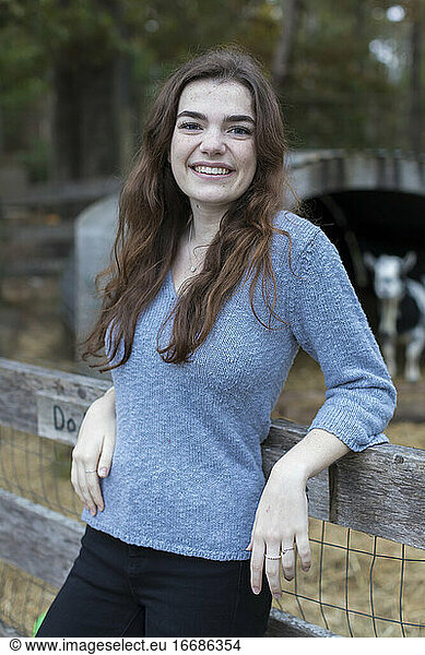 Portrait ot pretty teenage girl smiling at goat pen in farm setting