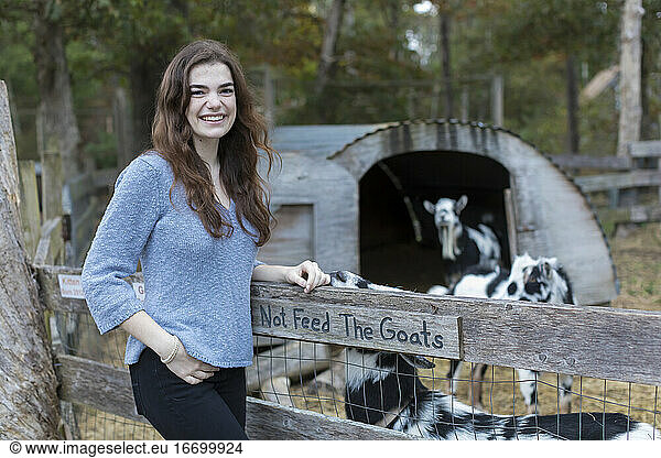 Portrait ot pretty teenage girl smiling at goat pen in farm setting