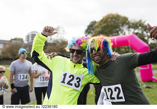 Portrait playful male runners wearing wigs and cheering at charity run in park