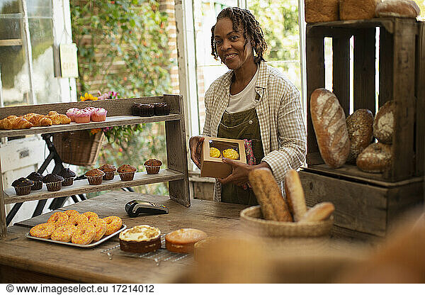 Portrait proud female baker boxing pastries in shop