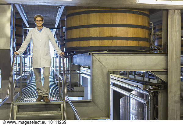 Portrait selbstbewusster Winzer im Laborkittel auf Plattform im Weinkeller