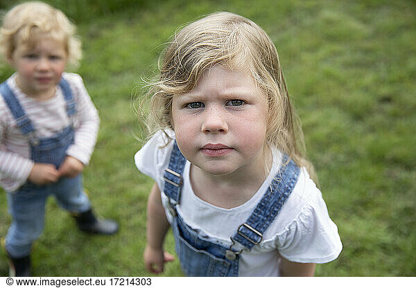 Portrait serious blonde girl in overalls with sister