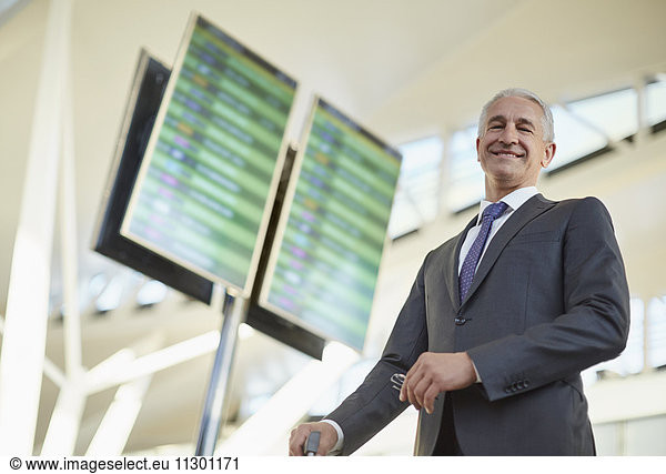 Portrait smiling businessman standing below arrival departure board in airport