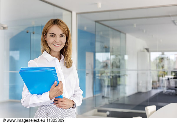 Portrait smiling businesswoman holding folders in conference room