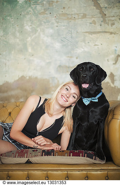 Portrait smiling  carefree young woman with black dog wearing bow tie on sofa