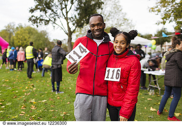 Portrait smiling  confident father and daughter runners with marathon bibs at charity run in park