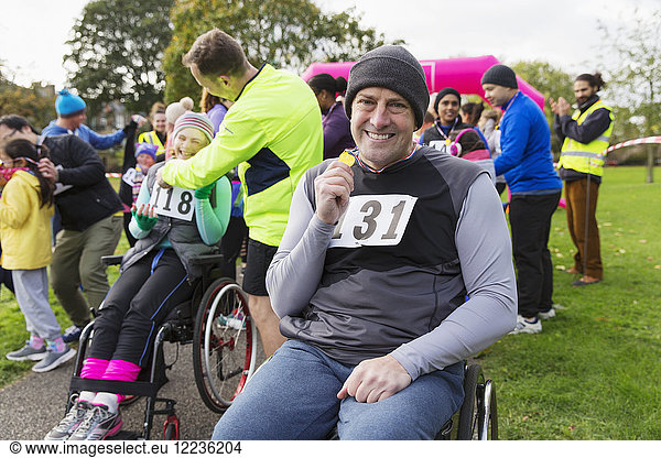 Portrait smiling  confident man in wheelchair showing medal at charity race in park
