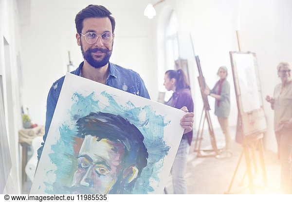 Portrait smiling  confident  proud male artist holding painting in art class studio