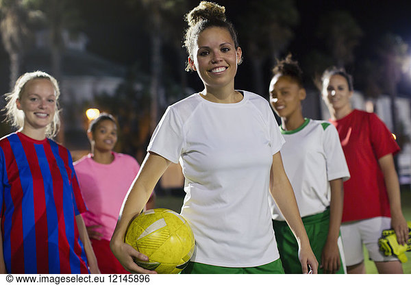 Portrait smiling  confident young female soccer team with ball on field at night