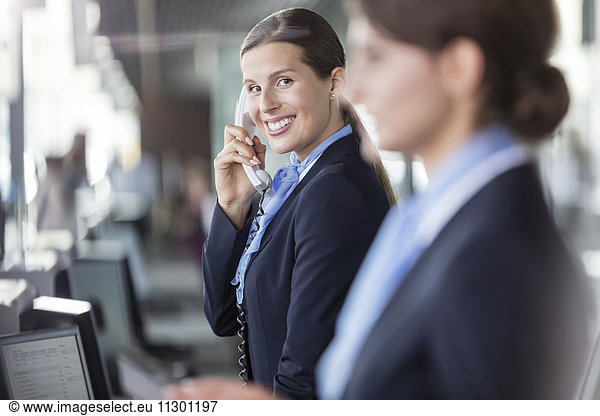 Portrait smiling customer representative talking on telephone at airport check-in counter