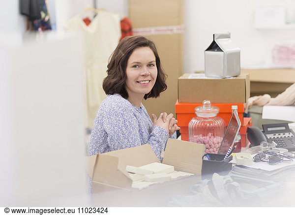 Portrait smiling fashion buyer at messy desk in office