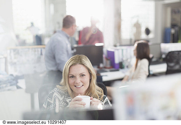 Portrait smiling fashion designer drinking coffee at computer in office