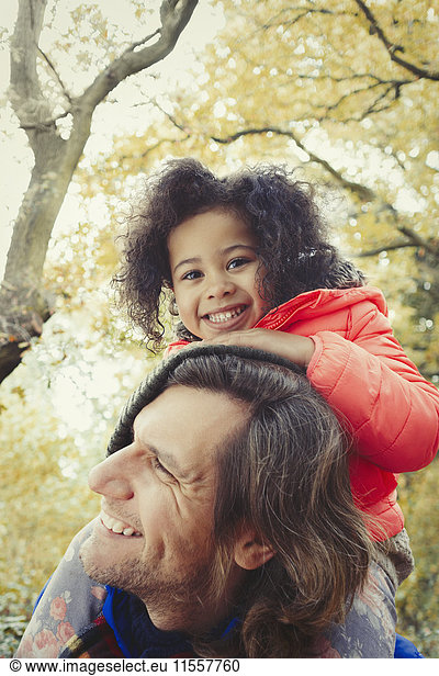 Portrait smiling father father carrying daughter on shoulders in autumn park