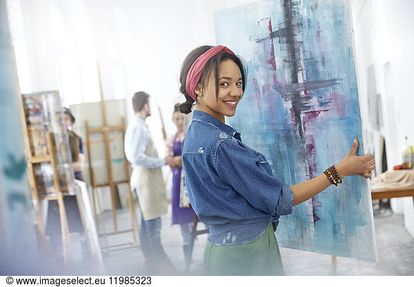 Portrait smiling female artist lifting painting in art class studio