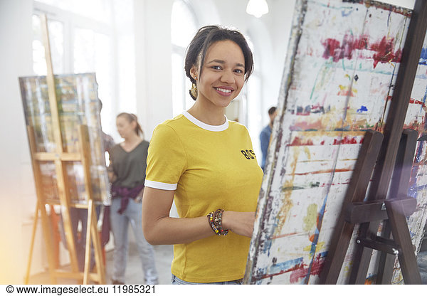 Portrait smiling female artist painting at easel in art class studio