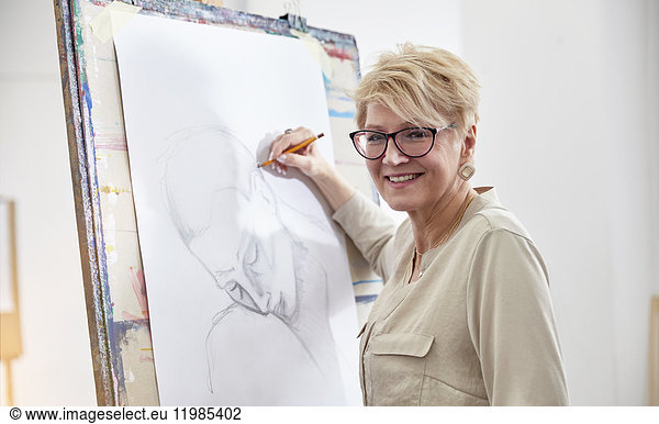 Portrait smiling female artist sketching at easel in art studio