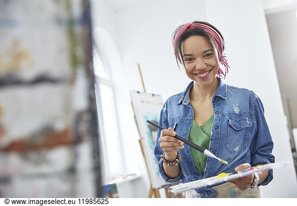 Portrait smiling female artist with paintbrush and palette  painting in art class studio