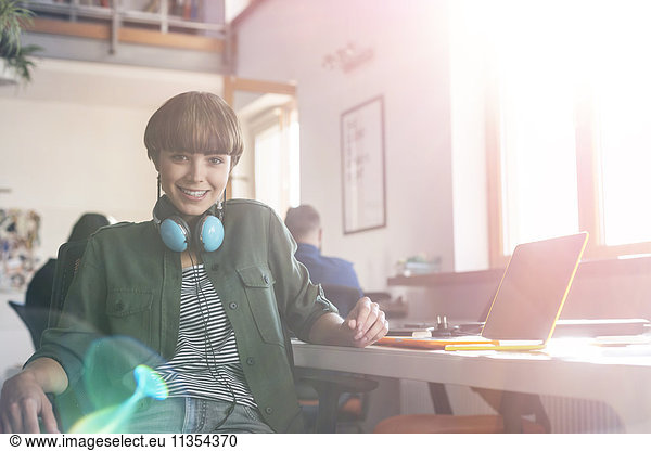 Portrait smiling female design professional with headphones at laptop in office