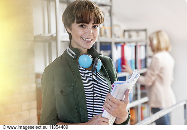 Portrait smiling female design professional with headphones holding paperwork in design library