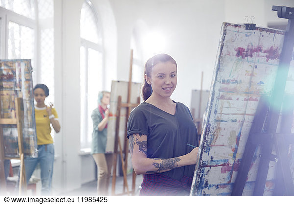 Portrait smiling female painter with tattoos painting in art class studio