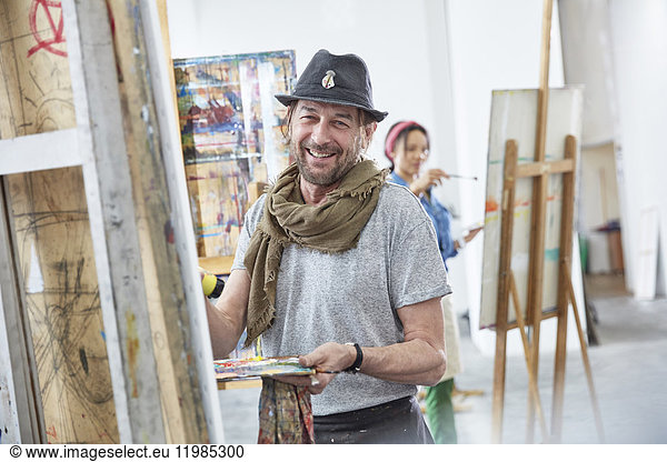 Portrait smiling male artist painting at easel in art class studio