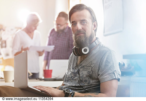 Portrait smiling male design professional with headphones using laptop in office