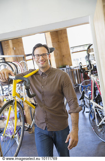 Portrait smiling man with eyeglasses carrying bicycle in bicycle shop
