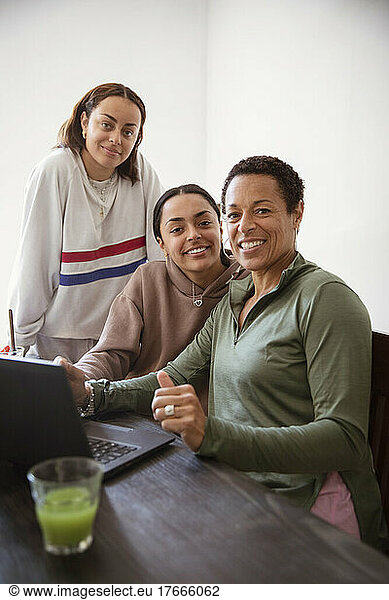 Portrait smiling mother and young adult daughters using laptop