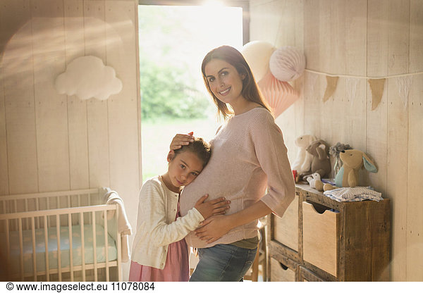 Portrait smiling pregnant mother and daughter in nursery