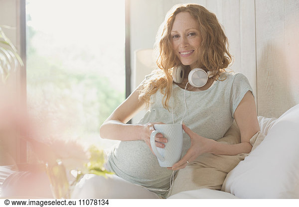 Portrait smiling pregnant woman with headphones drinking tea