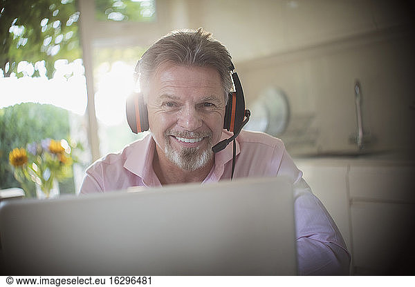 Portrait smiling senior man with headphones working at laptop