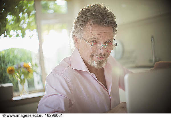 Portrait smiling senior man working at laptop in sunny kitchen